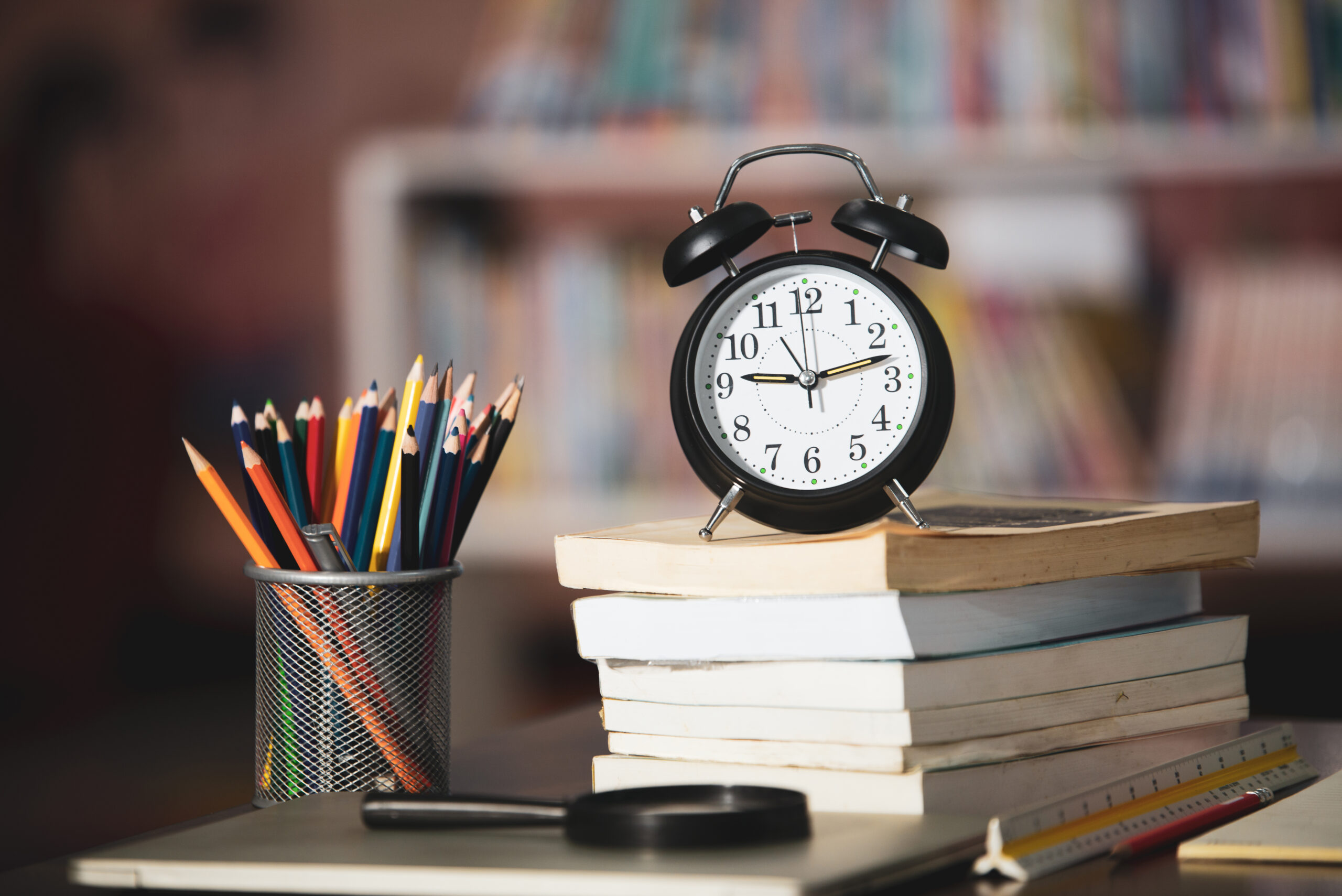 Book,laptop,pencil,clock on wooden table in library,education learning concept