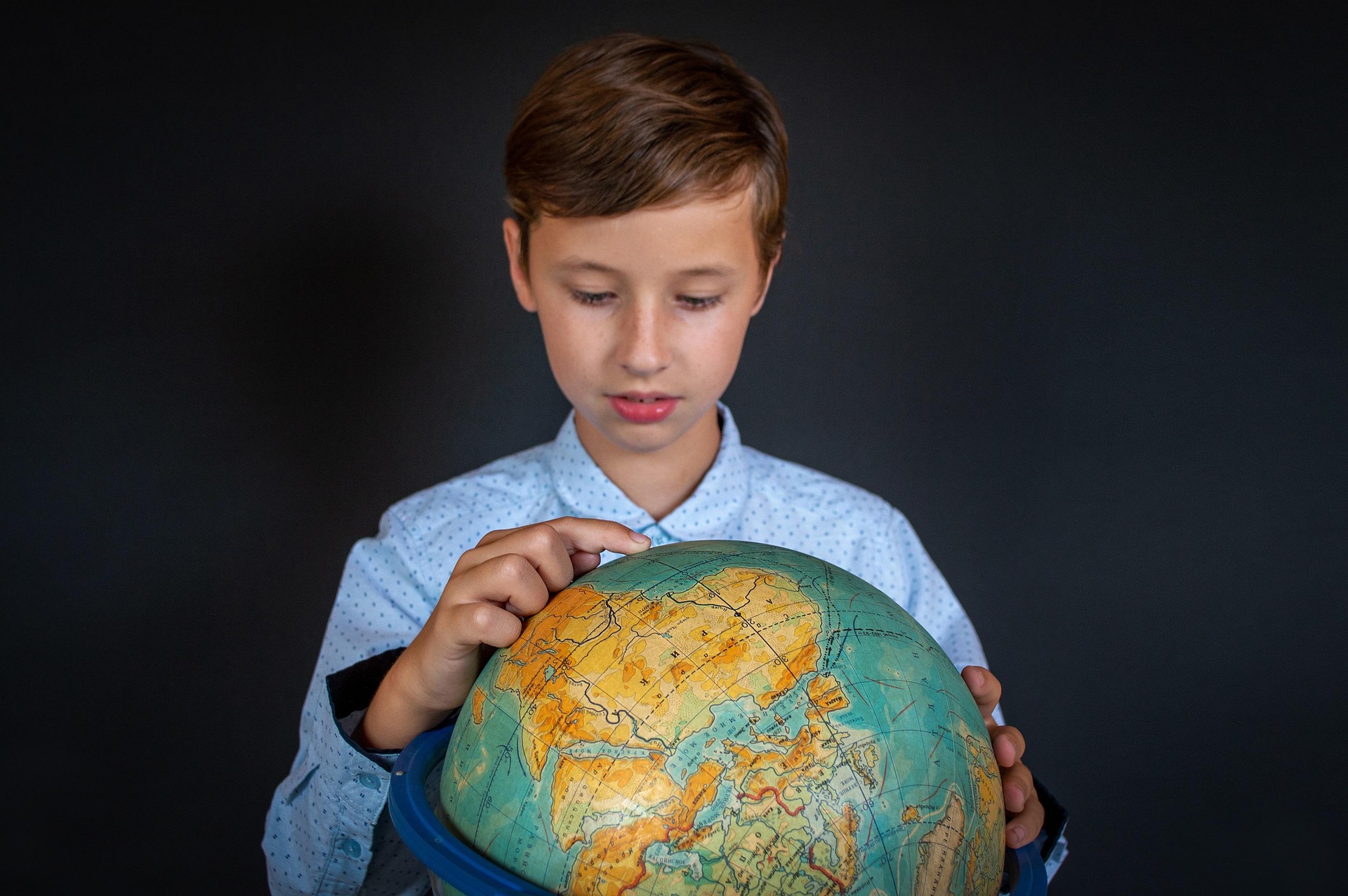 A boy is pointing his finger on the world globe.