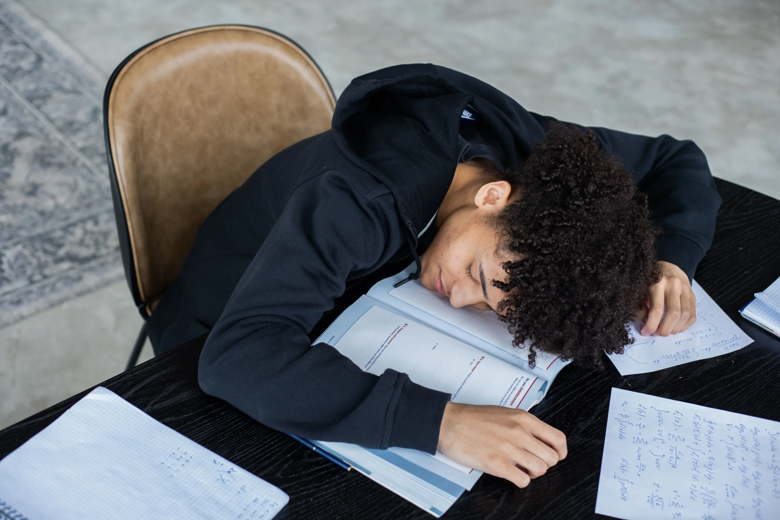 A boy is sleeping on the desk because of exam stress.